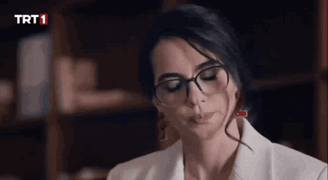 a woman wearing glasses is sitting in front of a bookshelf .