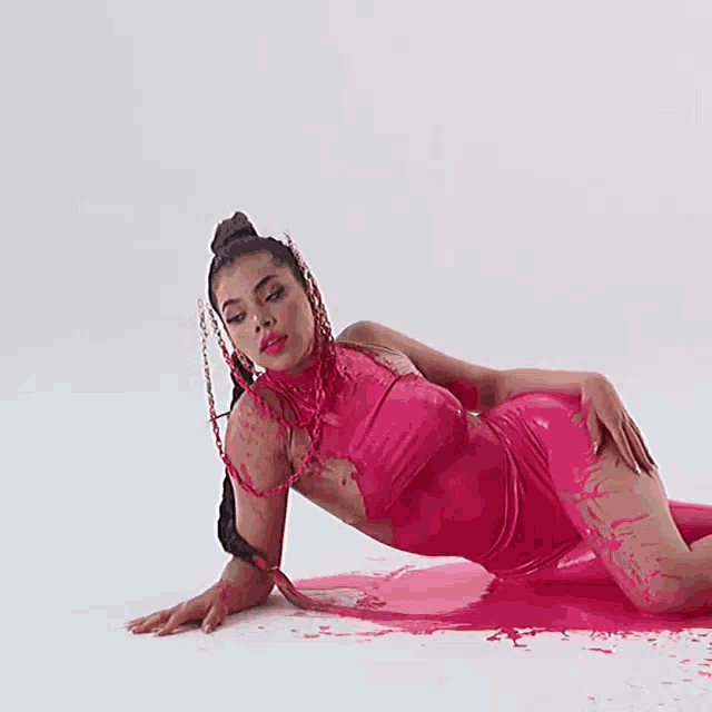 a woman in a pink bodysuit is laying on the floor in pink paint