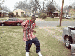 a man in a red white and blue shirt is dancing in front of a silver car