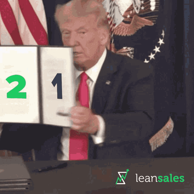 a man in a suit and tie holds up a sign with the number 2 on it