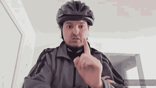 a man wearing a bicycle helmet and a gray jacket is making a funny face .
