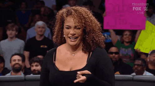 a woman with curly hair is laughing in front of a crowd while wearing a black top .
