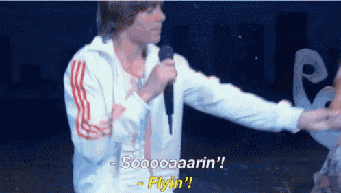 a man in a white jacket is holding a microphone and saying sooooaaaarin ! flyin !