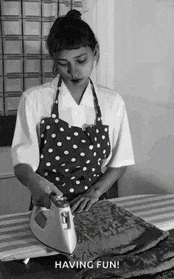 a woman in a polka dot apron is ironing a piece of fabric on an ironing board .
