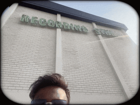 a man wearing sunglasses stands in front of a building that says recording studio