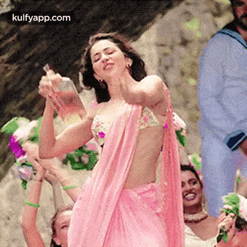 a woman in a pink saree is dancing with a group of people .