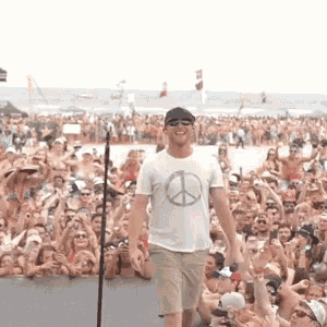 a man stands in front of a crowd wearing a peace sign shirt