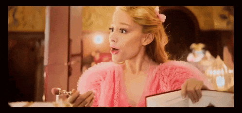 a woman in a pink dress is holding a bottle of perfume and a book .