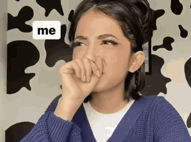 a woman in a blue sweater is covering her mouth with her hand in front of a cow print wall .