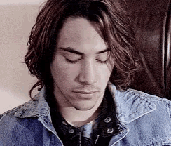 a man with long hair is wearing a blue denim jacket and looking down .
