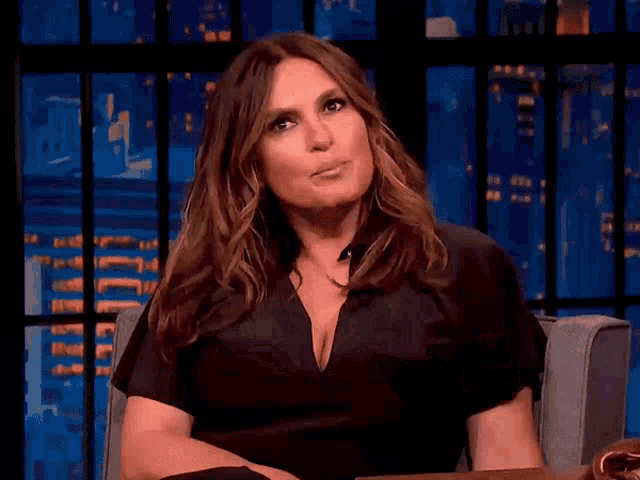 a woman in a black shirt is sitting in a chair with her hands on her chest