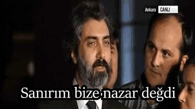 a man with a beard is surrounded by other men and says sanirim bize nazar degdi