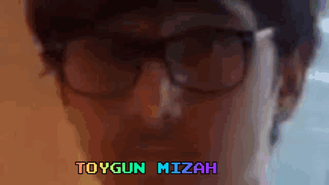 a close up of a man wearing glasses with the name toygun mizah written in the upper right corner