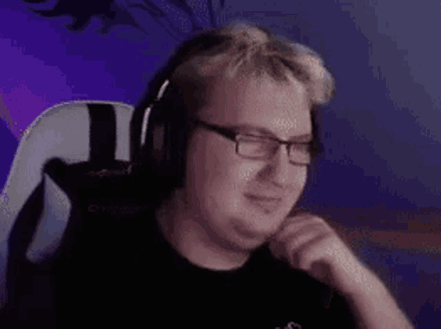 a man wearing headphones and glasses is sitting in a chair in front of a computer screen .