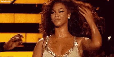 a woman in a gold dress is dancing on a stage while holding her hair .