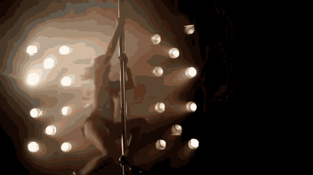 a woman is dancing on a pole in front of a crowd of lights .