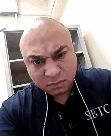 a bald man wearing a shirt that says sbtc looks angry
