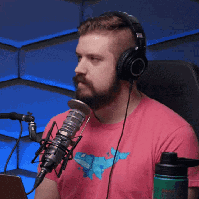 a man wearing headphones and a pink shirt with a shark on it is sitting in front of a microphone