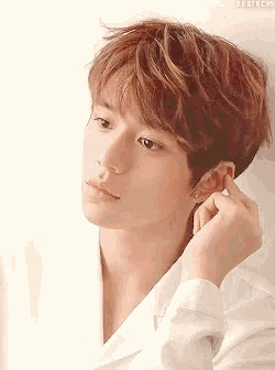a young man is adjusting his earring with his hand .