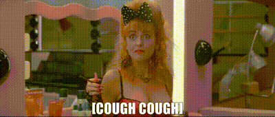 a woman with a bow on her head is looking at herself in a mirror and says " cough cough "