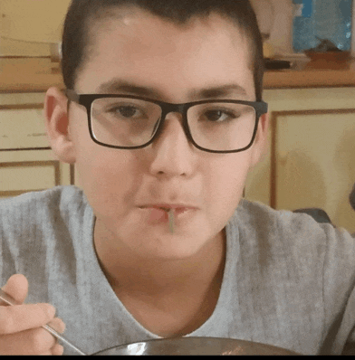 a boy wearing glasses is eating from a bowl with a fork