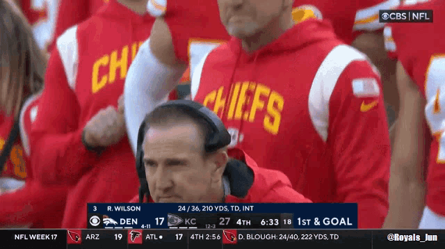 a man wearing a chiefs sweatshirt watches a game on cbs