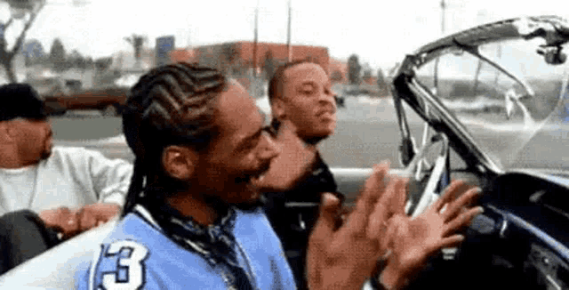 snoop dogg is sitting in the back seat of a convertible car with other men .