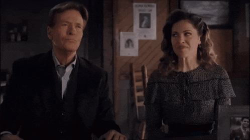 a man and a woman sit at a table with a wanted poster on the wall
