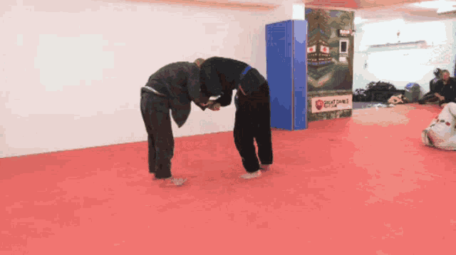 two men are wrestling in a gym with a sign that says ' karate ' on it