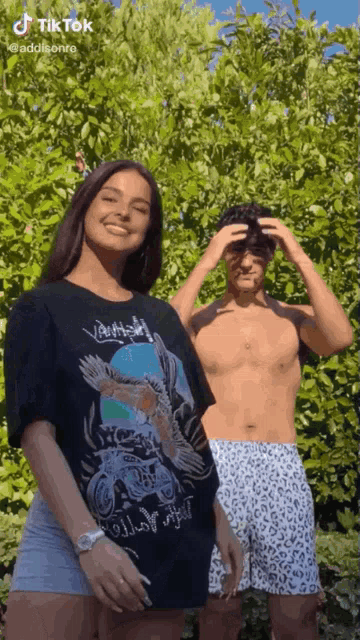 a man and a woman are standing next to each other in front of a tree .