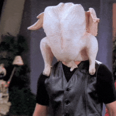 a man with a turkey on his head is wearing a black vest