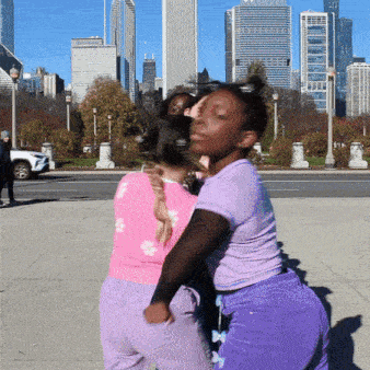 a girl in a pink top and purple shorts is hugging another girl in front of a city skyline