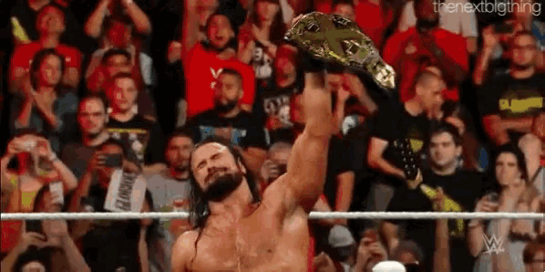 a wrestler is holding a championship belt over his head in front of a crowd of people .