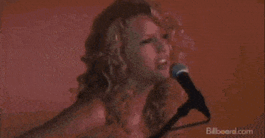 a naked woman is singing into a microphone while playing a guitar .