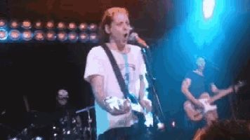a man singing into a microphone while playing a guitar on a stage