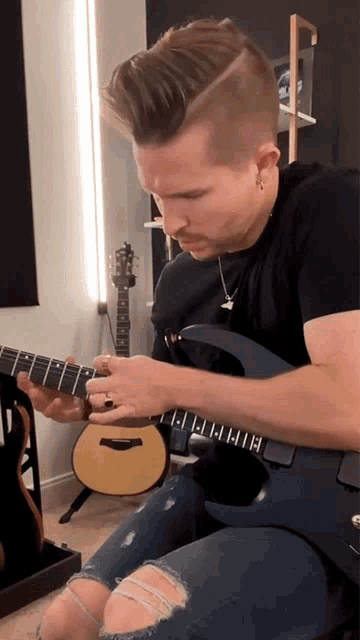 a man in a black shirt is playing a guitar with the letter h on the fretboard