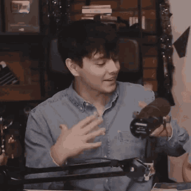 a man in a denim shirt is sitting in front of a microphone and talking .