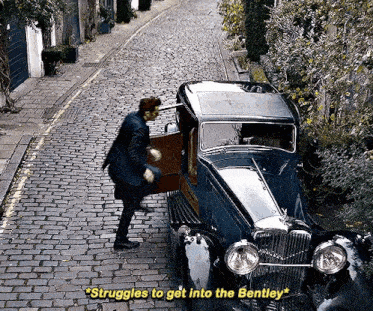 a man standing next to a bentley car on a cobblestone road