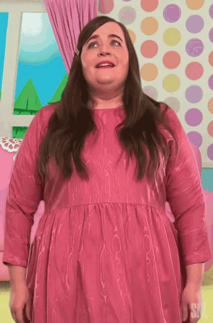 a woman in a pink dress is standing in front of a colorful polka dot wall