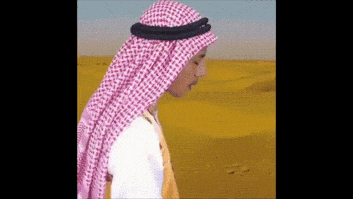 a man wearing a pink and white checkered head scarf is standing in the desert