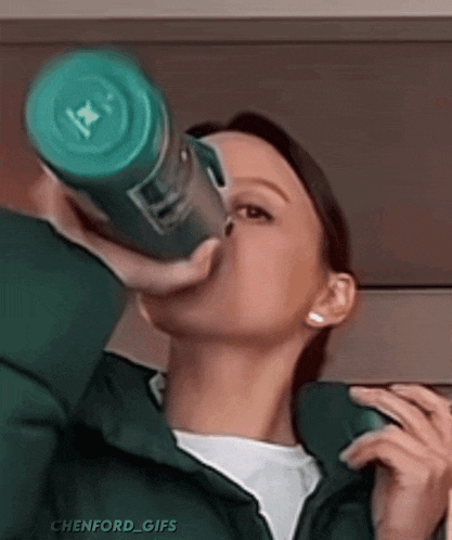 a woman is drinking water from a green bottle