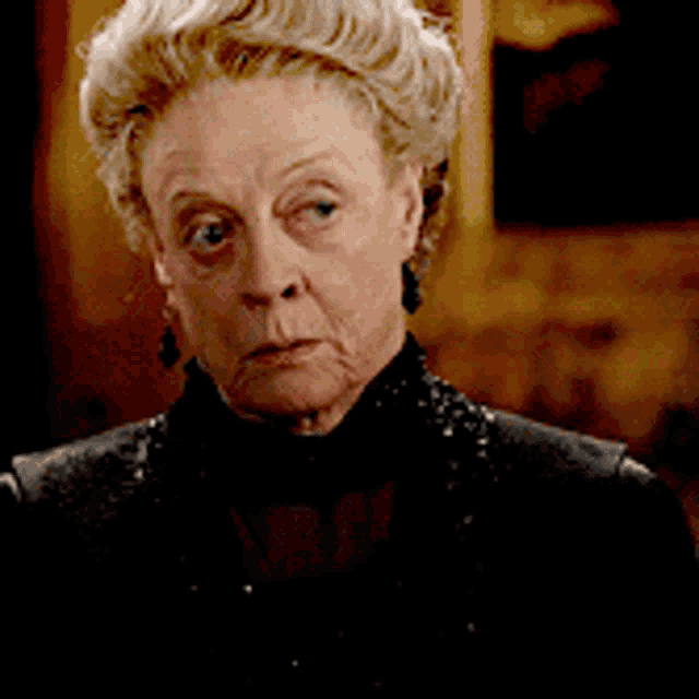 an older woman wearing earrings and a black jacket looks at the camera