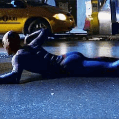 a man in a spiderman costume is laying on the ground in front of a yellow taxi