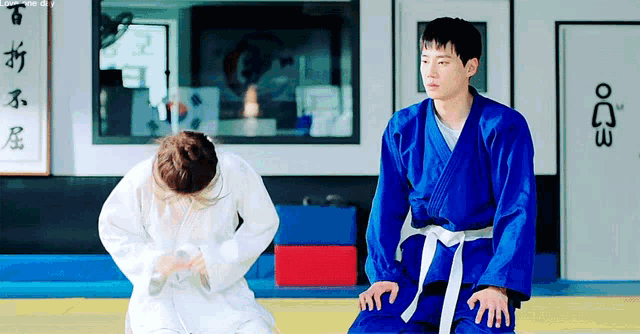 a man in a blue karate uniform sits next to a woman in a white robe in a gym .