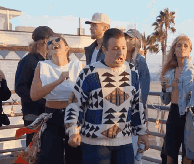 a group of people are standing on a balcony and one of them is wearing a blue and white sweater with triangles on it