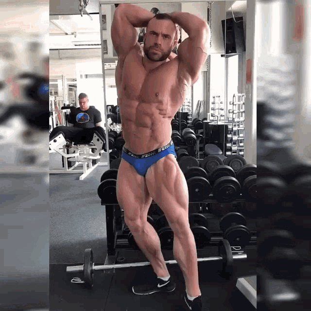 a bodybuilder in a blue underwear stands in front of a mirror