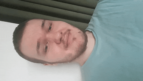 a man with a beard and a blue shirt is laying on a bed