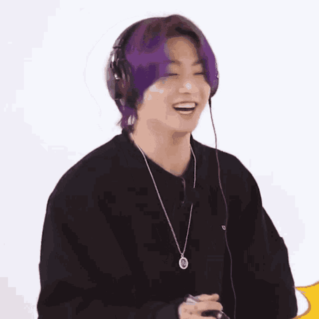 a young man with purple hair is wearing headphones and a necklace while smiling .