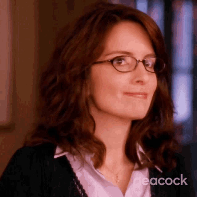 a close up of a woman wearing glasses and a peacock logo in the background .