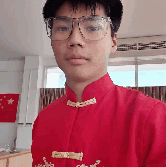 a young man wearing glasses and a red shirt stands in front of a china flag